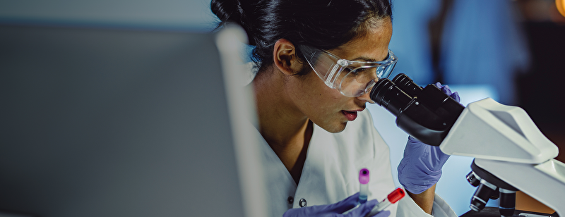 Laboratory researcher is looking through a microscope.