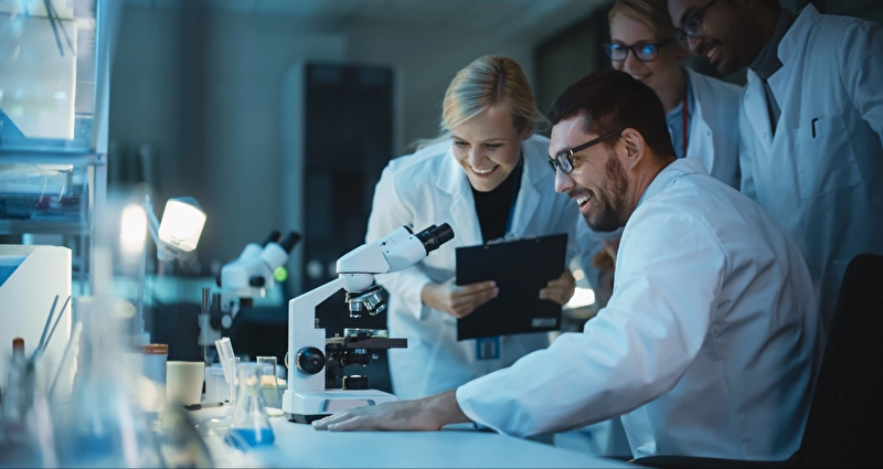 Four excited scientists looking through a microscope